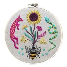 pink, yellow, and turquoise flowers and garden animals embroidered on gray fabric in a hoop