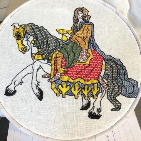 An embroidery of a long-haired man holding a golden bowl while riding on an armored horse, done in a medieval style and still inside the embroidery hoop