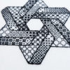 Close-up of the corner of a hexagram made from two intersecting Penrose triangles stitched in blackwork patterns on white canvas.