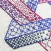 Close-up of the corner of a hexagram made from two intersecting Penrose triangles stitched in purple blackwork patterns on white canvas.