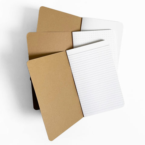 Three blank notebooks with kraft brown covers propped open to show blank, lined, and dotted grid interior pages