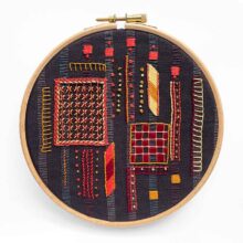 warm colored stitches embroidery sampler on dark gray striped fabric in a hoop