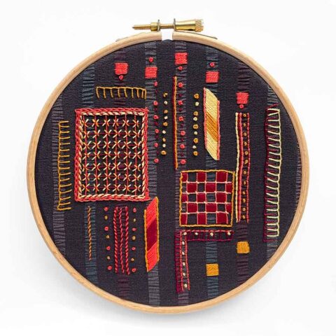 warm colored stitches embroidery sampler on dark gray striped fabric in a hoop