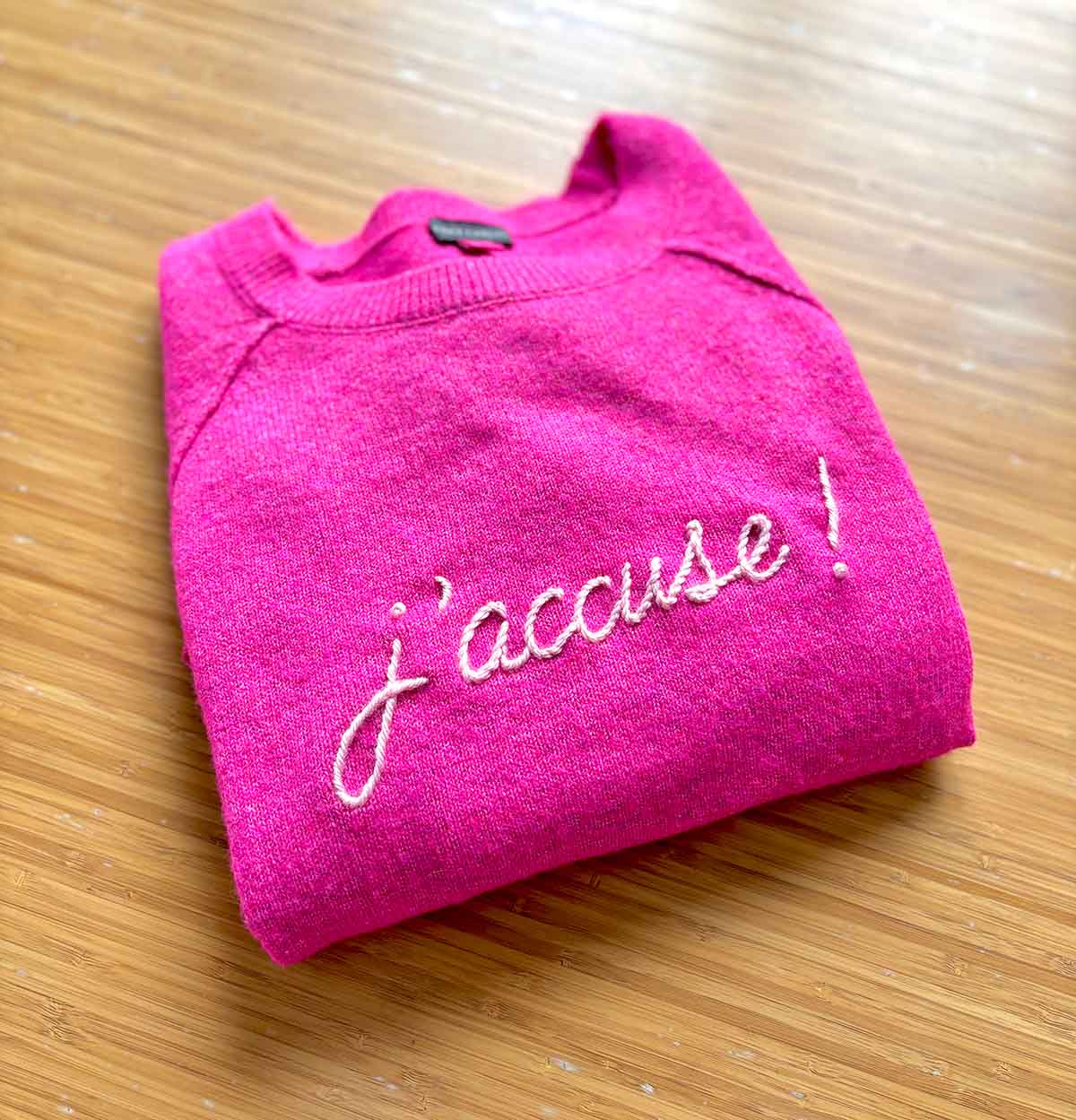 j'accuse embroidered on a bright pink sweater