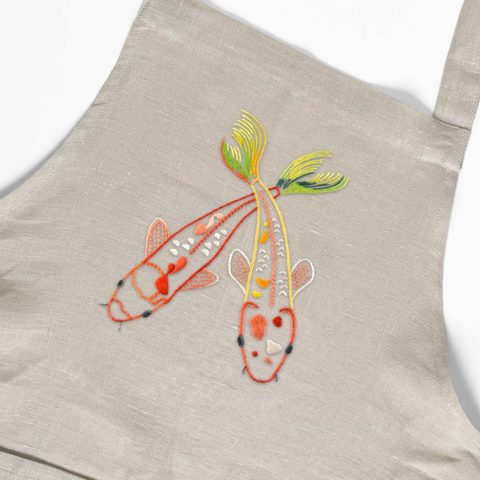 close up of the bib of a natural linen apron embroidered with two orange and green koi fish