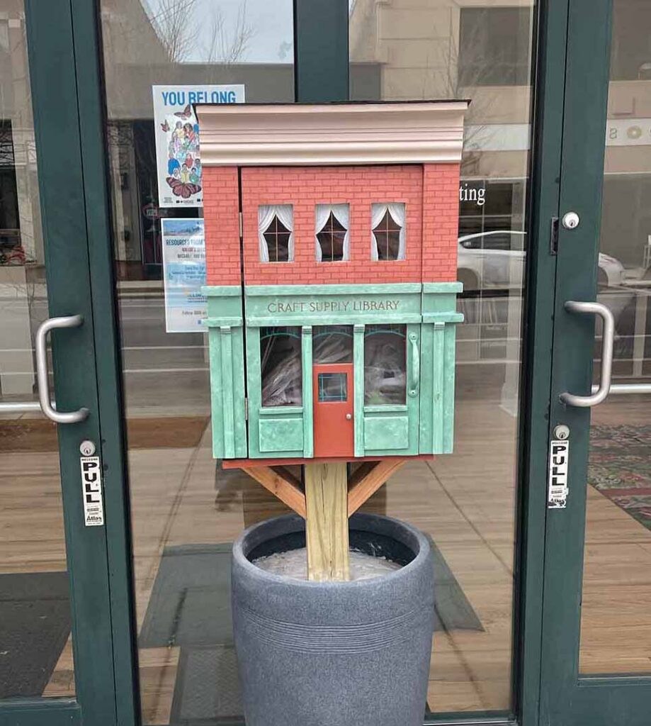 A miniature brick house filled with free craft supplies mounted on a sidewalk