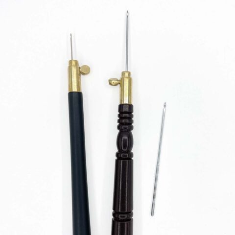 two dark wooden tambour handles showing needles inserted at different lengths next to a loose needle