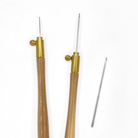 two natural wooden tambour handles showing needles inserted at different lengths next to a loose needle