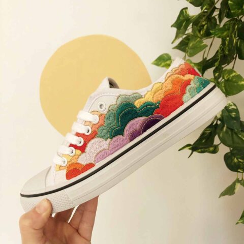 A white canvas sneaker embroidered with layered multicolored clouds