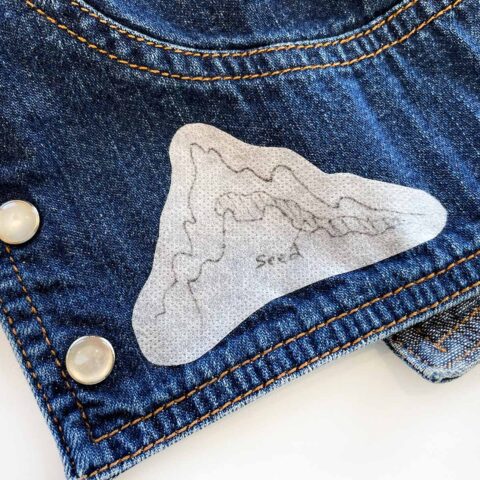 a hand-drawn mountain embroidery pattern on stabilizer stuck on the cuff of a denim jacket