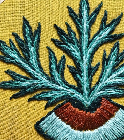close-up of ochre fabric embroidered with a mugwort plant blooming up from the center of an eye