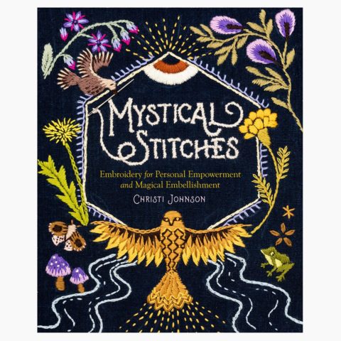 A black book cover with the title "Mystical Stitches" in white, surrounded by embroidered symbols of the natural world in purple, green, and gold