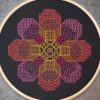 A blackwork embroidery of a flower shape made out of eight octagons filled with various stitch patterns in warm tones on black fabric