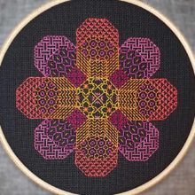A blackwork embroidery of a flower shape made out of eight octagons filled with various stitch patterns in warm tones on black fabric