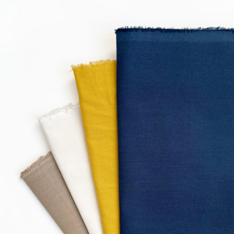folded cotton broadcloth fabric in light brown, cream, ochre, and slate blue arrange in a fan