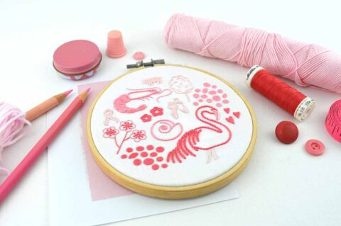 Several folk art objects embroidered in pink in a wooden hoop