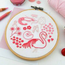 Several folk art objects embroidered in pink in a wooden hoop