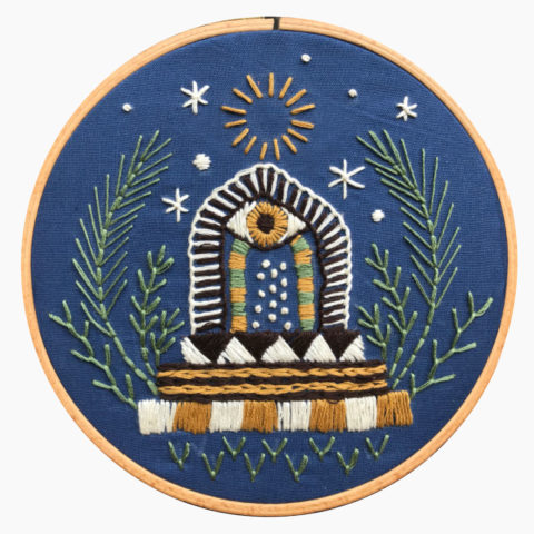 royal blue fabric in a wooden embroidery hoop stitched with images of a portal door with an eye on top surrounded by plants and stars