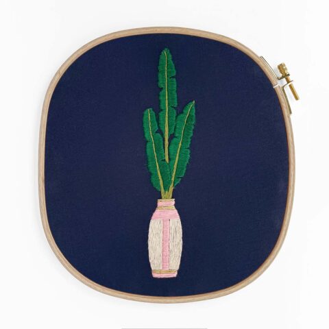 a potted palm house plant in a tall white and pink vase embroidered on navy fabric