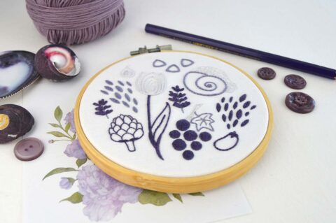 Several folk art objects embroidered in purple in a wooden hoop