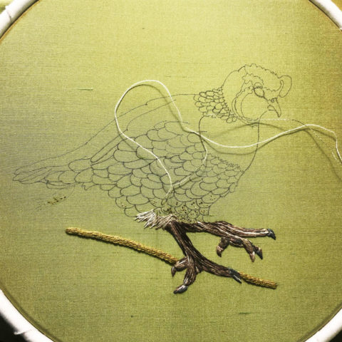 A quail drawn on olive green silk inside an embroidery hoop with the feet stitched in brown