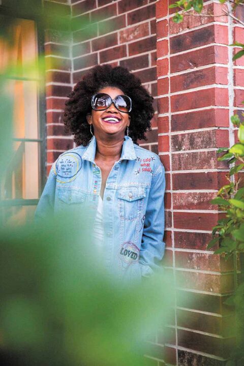 artist and author bianca springer wearing big sunglasses and smiling in front of a brick wall