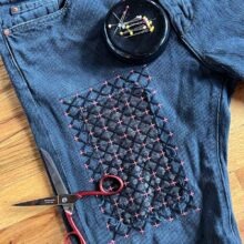 A pair of jean shorts mended on one leg with a patch and sashiko embroidery stitching
