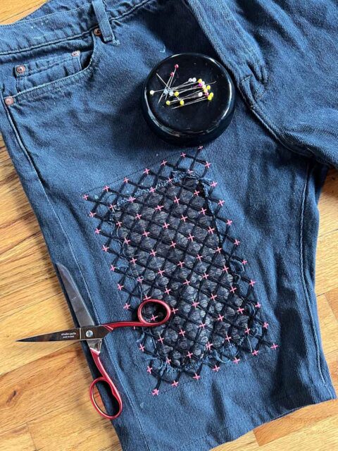 A pair of jean shorts mended on one leg with a patch and sashiko embroidery stitching