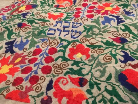 close-up of colorful botanical folk art patterns cross-stitched around the hebrew words shabbat shalom