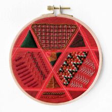 an embroidery sampler showing different stitches filling in triangular areas of red fabric