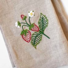 A small spray of strawberries with flowers and leaves embroidered on a natural linen tea towel