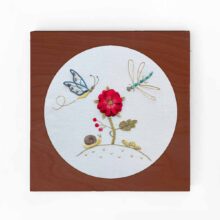 stumpwork flower and insect embroidery inside a square wood hoop frame with caramel stain finish