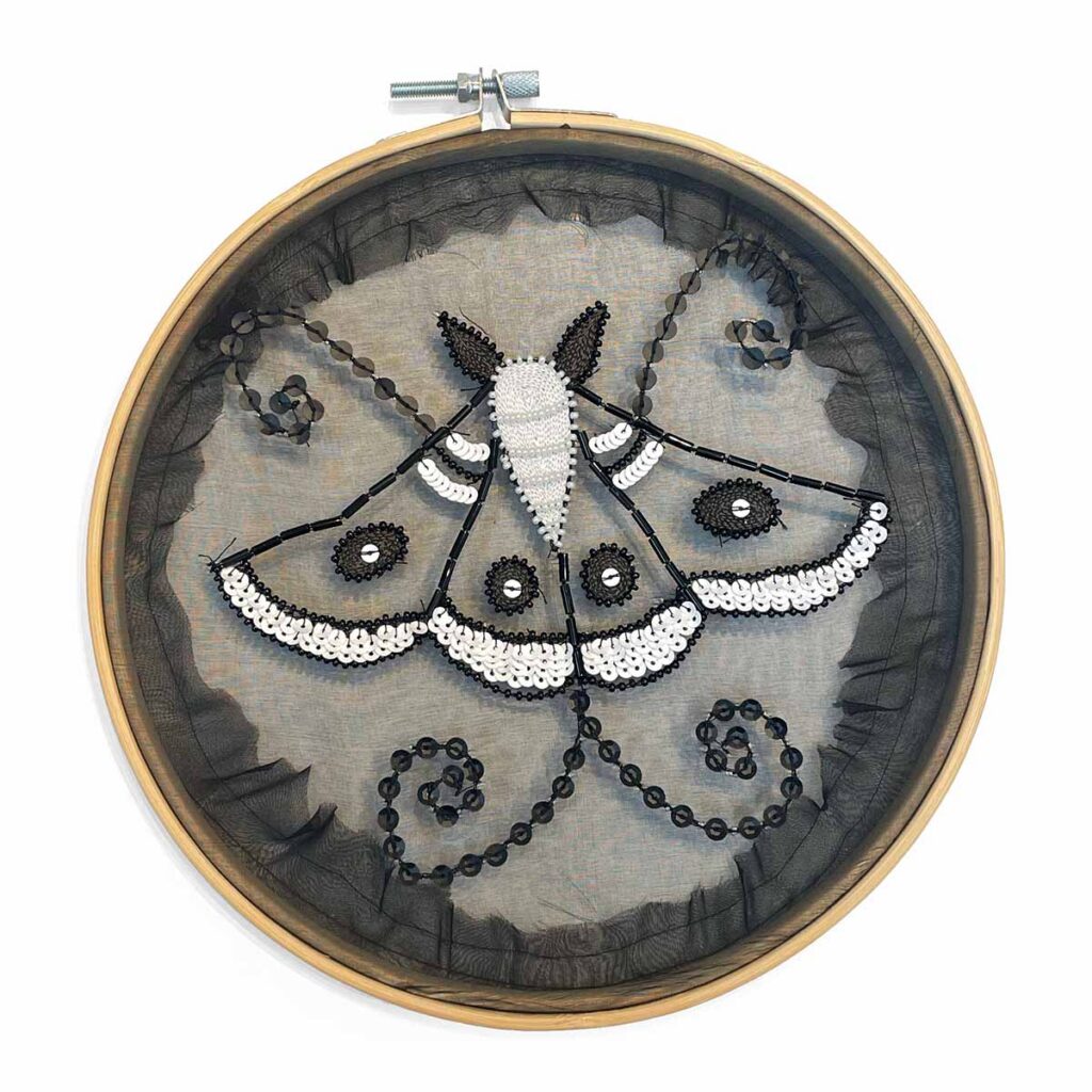 black and white moth embroidered in beads and sequins on black organza in an embroidery hoop