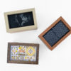 three wooden boxes with frame lids displaying pieces of embroidered needlework