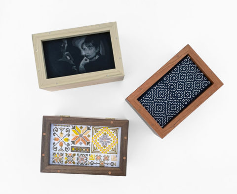 three wooden boxes with frame lids displaying pieces of embroidered needlework