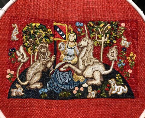 A very detailed embroidery resembling a flemish tapestry showing a lady seated with a lion and a unicorn