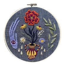 a yellow vase with flowers and surrounded by mystical symbols embroidered on dark blue fabric in a hoop