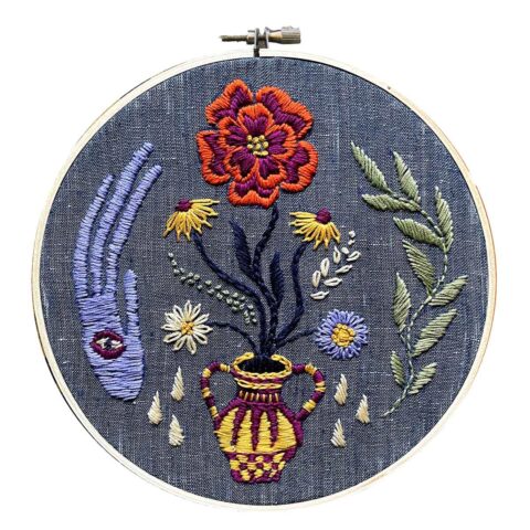 a yellow vase with flowers and surrounded by mystical symbols embroidered on dark blue fabric in a hoop