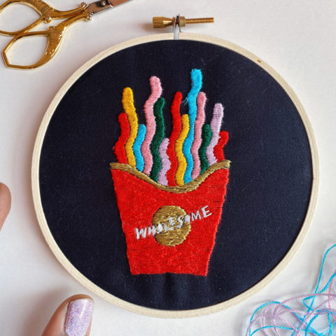 embroidery pattern composed of a box of colorful, squiggly French fry like shapes and text that reads “Wholesome”