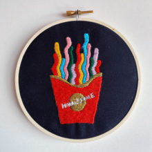 embroidery pattern composed of a box of colorful, squiggly French fry like shapes and text that reads “Wholesome”